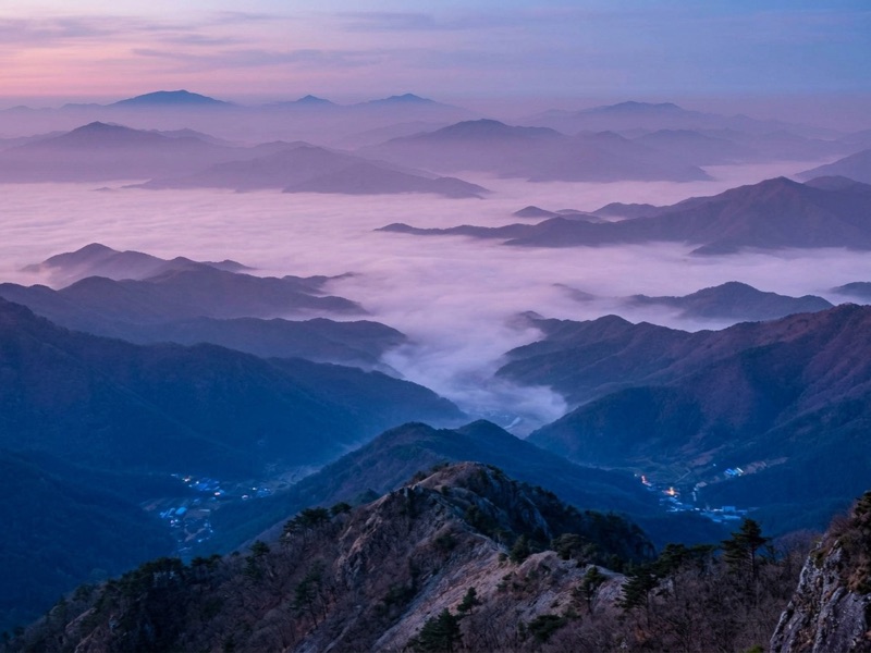 Layered mountain ridges rising above a valley of clouds at dawn