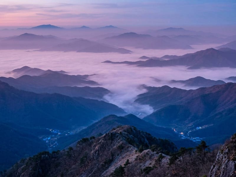 Layered mountain ridges rising above a valley of clouds at dawn
