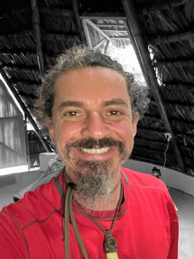 Benjamin Peace Hoffman smiling in a red shirt under a thatched roof