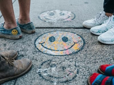 Chalk smiley faces drawn on pavement surrounded by several people's sneakers
