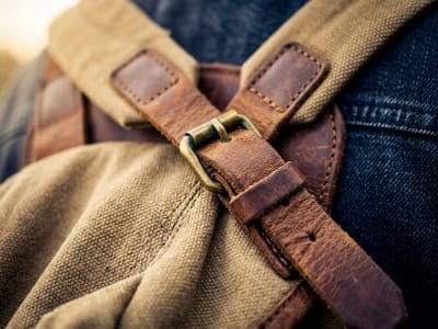 Close-up of a leather strap and buckle on a canvas backpack worn over denim