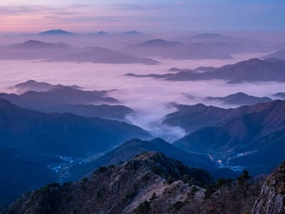 Layered mountain ridges rising above a valley of clouds at dawn