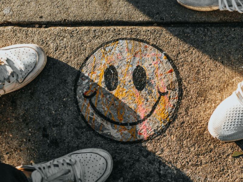 Colorful smiley face with paint drips painted on a sidewalk, surrounded by sneakers