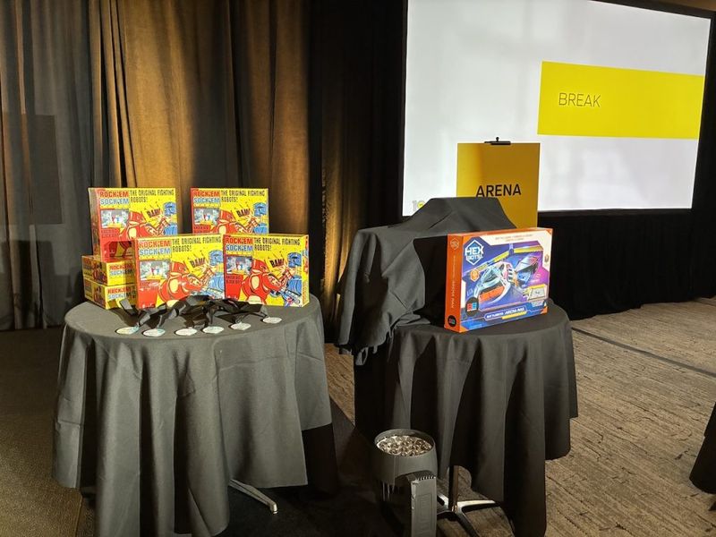 Rock Em Sock Em Robots game boxes and a Hex Bugs Battlebots Arena Max kit displayed on tables at a Battle Bots team-building event venue