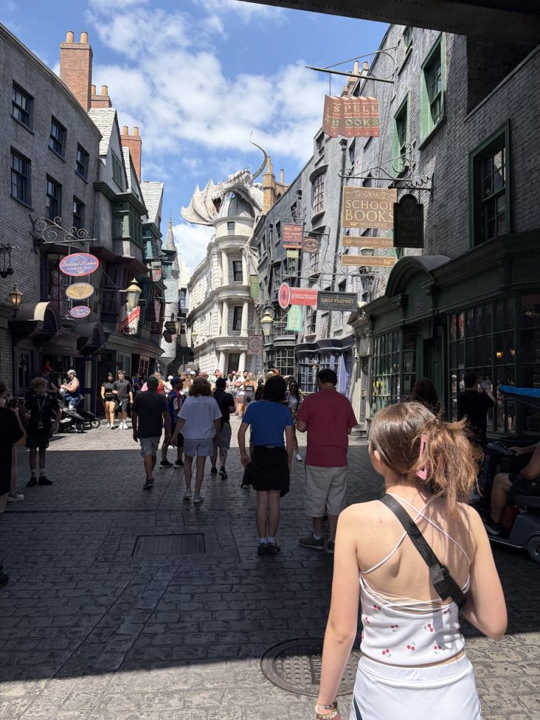 Visitors walking the cobblestone street of Diagon Alley at the Wizarding World of Harry Potter, Universal Studios, with the Gringotts dragon visible above the shops