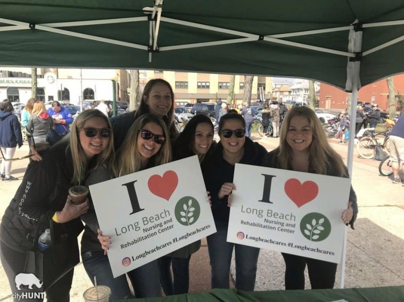 cityHUNT participants at the 2019 Long Beach Chamber of Commerce event holding I Love Long Beach Nursing and Rehabilitation Center signs at an outdoor booth