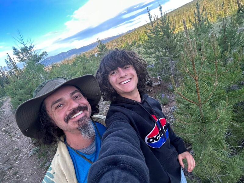 Ben Hoffman and his son smiling on a mountain hike surrounded by pine trees