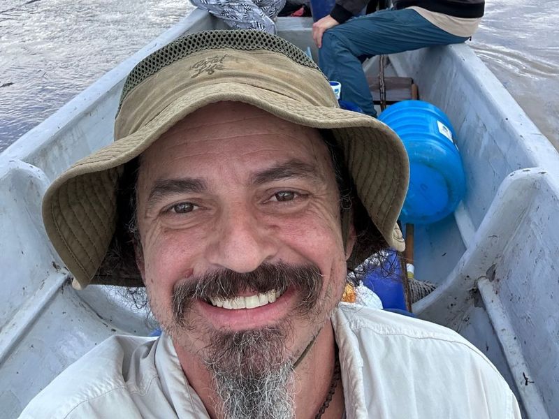 Ben Hoffman smiling in a wooden river boat, wearing a khaki bucket hat