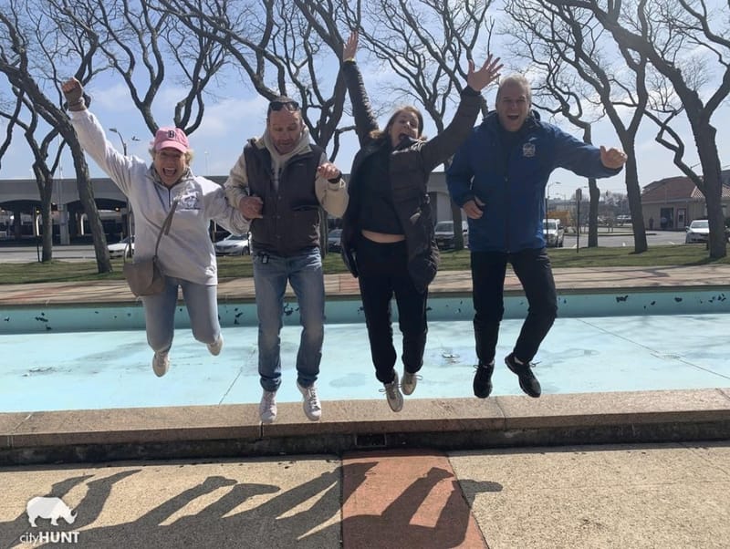 Four teammates jumping in the air together in front of a fountain