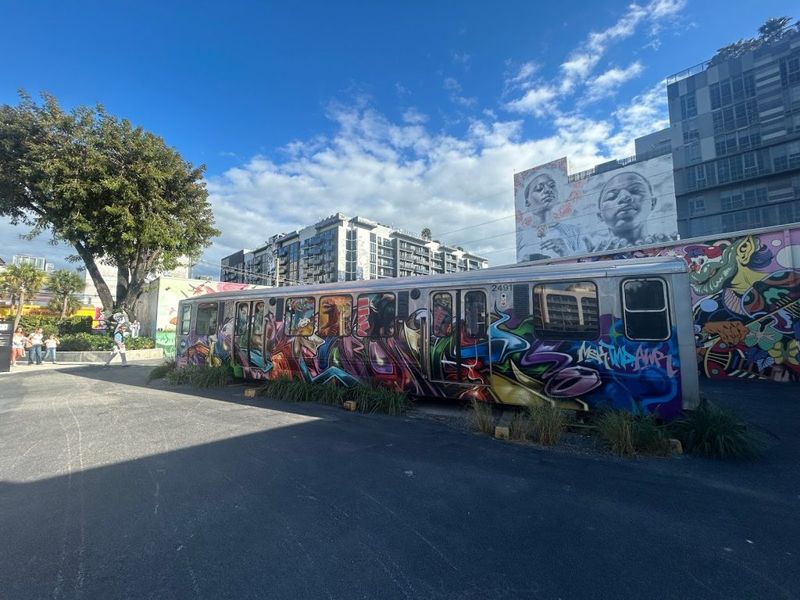 Graffiti-covered subway car in an urban street art district, with a large portrait mural on a building behind it