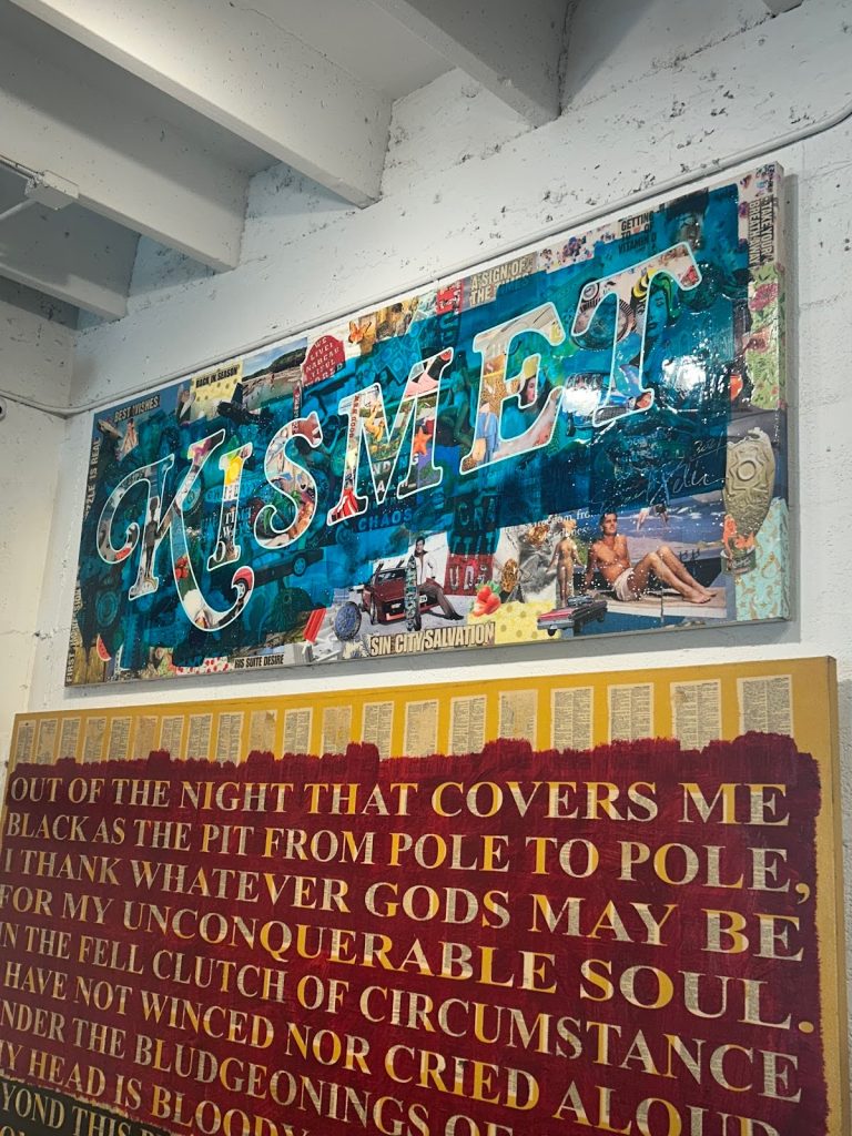 Two mixed-media artworks on a white wall: a colorful collage piece spelling KISMET in teal letters above a text painting featuring opening lines from the poem Invictus
