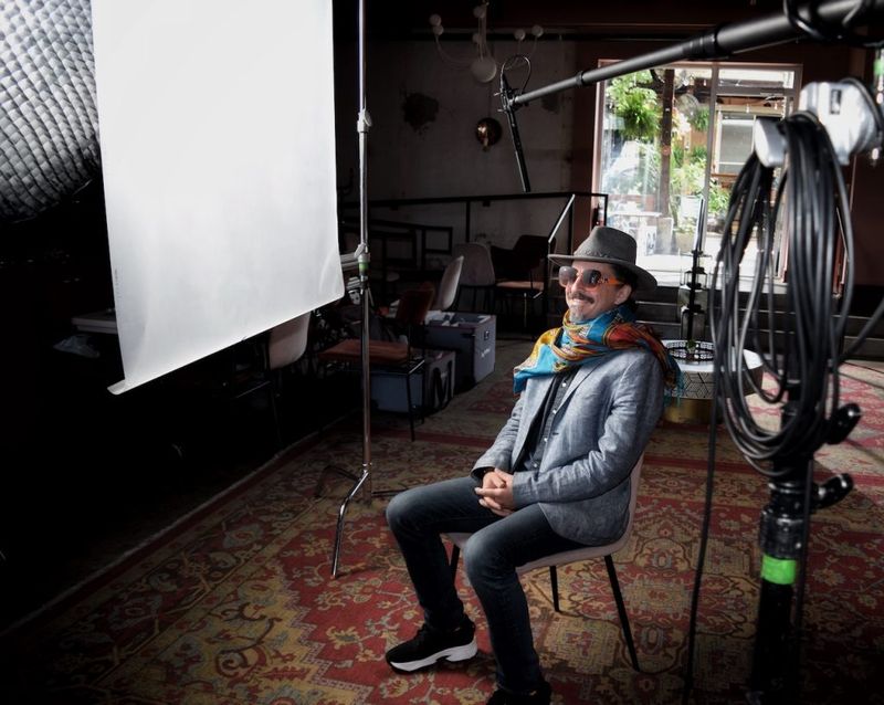 Ben Hoffman seated during a Nashville video shoot, wearing a wide-brim hat, colorful scarf, and sunglasses, with studio lighting and a boom mic visible